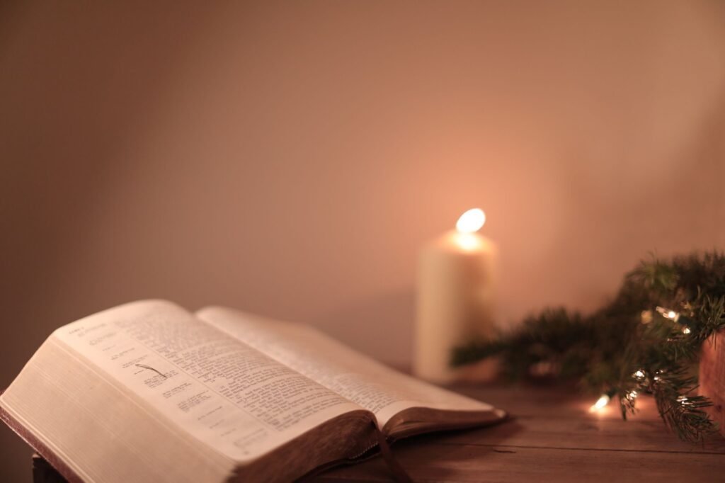 An open Bible beside a lit candle in soft evening light