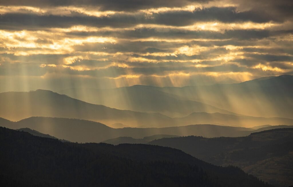 Rays of sunlight breaking through clouds over layered mountain ranges