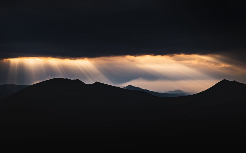 Rays of light breaking through darkness over the mountains