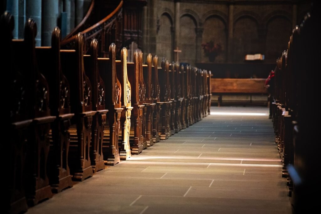 Warm light falling across the aisle of a quiet church between wooden pews